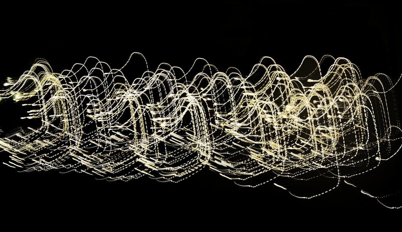 Dynamic abstract image of light trails creating wave-like patterns against a dark backdrop.