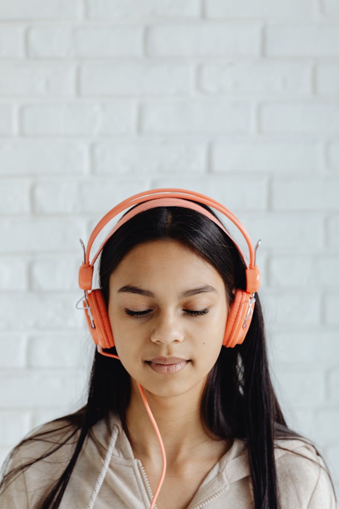 Brunette woman with eyes closed enjoying music wearing orange headphones indoors.